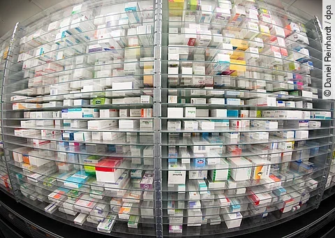 Regale einer Apotheke, dicht gefüllt mit Medikamentenschachteln in verschiedenen Farben und Größen.