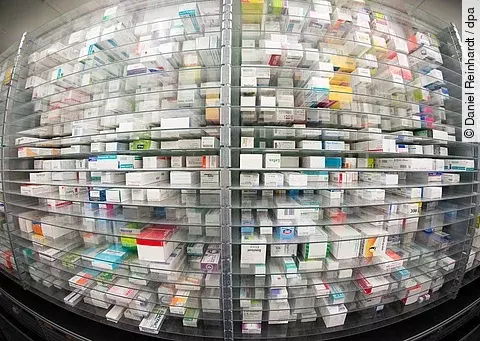 Regale einer Apotheke, dicht gefüllt mit Medikamentenschachteln in verschiedenen Farben und Größen.