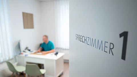 Ein Hausarzt sitzt in einem Sprechzimmer seiner Hausarztpraxis an einem Schreibtisch und arbeitet am Computer. Ein Hausarzt sitzt in einem Sprechzimmer seiner Hausarztpraxis an einem Schreibtisch und arbeitet am Computer.