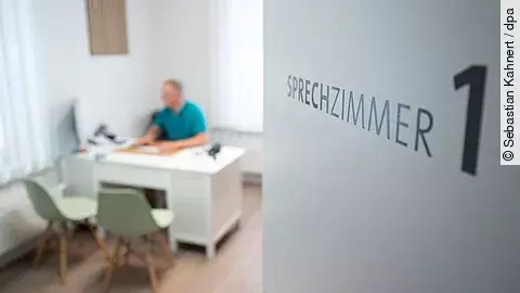 Ein Hausarzt sitzt in einem Sprechzimmer seiner Hausarztpraxis an einem Schreibtisch und arbeitet am Computer. 