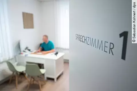 Ein Hausarzt sitzt in einem Sprechzimmer seiner Hausarztpraxis an einem Schreibtisch und arbeitet am Computer.