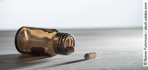 Ein Glasfläschchen mit mehreren Medikamenten liegt auf einem Tisch. Der Hintergrund ist weiß.