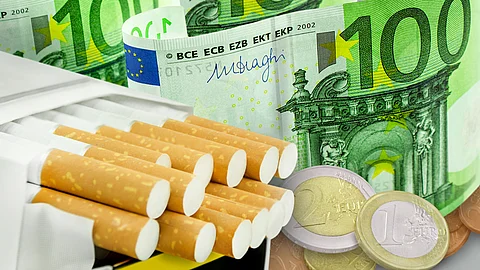 1 Schachtel Zigaretten und Euro Mehrere Zigaretten in einer Zigarettenschachtel liegen vor und auf Euro-Banknoten und Münzen,