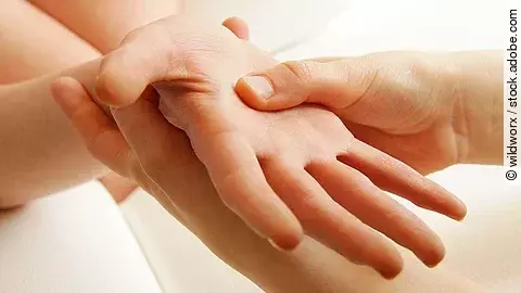 Nahaufnahme zweier Hände, bei der eine Handfläche durch sanften Druck mit den Fingern der anderen Hand stimuliert wird 