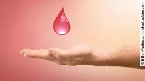 Eine ausgestreckte Hand hält einen roten Blutstropfen vor einem sanften rosa Hintergrund