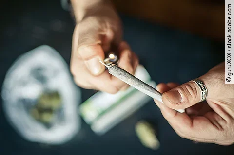 Close up of addict lighting up marijuana joint with lighter