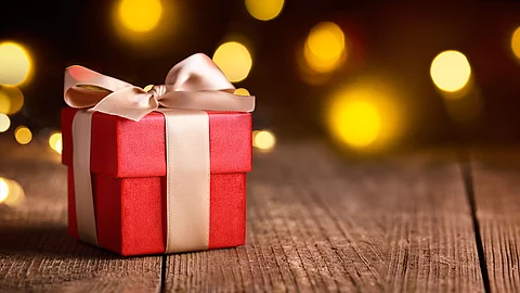 Rotes Geschenk mit heller Schleife auf Holzoberfläche, im Hintergrund warme, unscharfe Lichter.