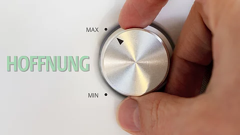 Eine Hand dreht an einem silberfarbenen Drehknopf, der mit einer niedrigen und einer hohen Einstellung markiert ist; links davon steht in grüner Schrift das Wort „HOFFNUNG“.