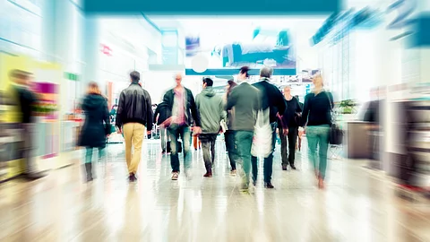 Menschen gehen durch ein Einkaufszentrum mit Geschäften und breiten Laufwegen.