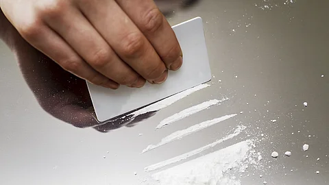 Eine Hand zieht mit einer Plastikkarte mehrere Linien aus weißem Pulver auf einer glatten Oberfläche.