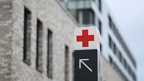 Ein Wegweiser mit rotem Kreuz-Symbol vor einem unscharfen Krankenhausgebäude aus Backstein und moderner Fassade