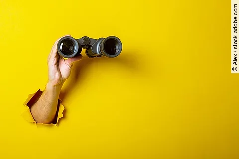 Female hand holds black binoculars on a yellow background. Looki