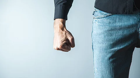Androhung von körperlicher Gewalt: Nahaufnahme eines Unterkörpers und eines Arms, bei dem eine Faust angespannt nach unten zeigt 
