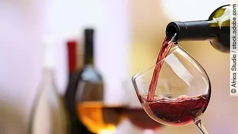 Weinflaschen und Weingläser auf einem Tisch; ein Weinglas wird aktuell befüllt..