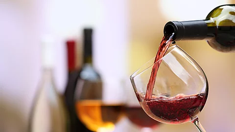 Weinflaschen und Weingläser auf einem Tisch; ein Weinglas wird aktuell befüllt..