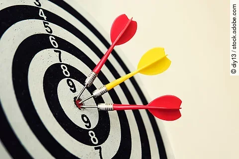 Side view of a dartboard with three darts in the bull's eye. Wel