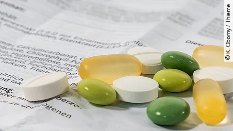 Verschiedene Tabletten und Kapseln liegen auf einem aufgefalteten, bedruckten Beipackzettel.