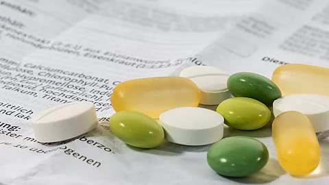 Verschiedene Tabletten und Kapseln liegen auf einem aufgefalteten, bedruckten Beipackzettel.