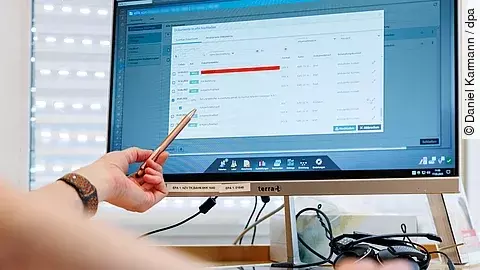 Eine Person zeigt mit einem Stift auf einen Computerbildschirm, auf dem eine digitale Patientenakte mit medizinischen Dokumenten geöffnet ist.