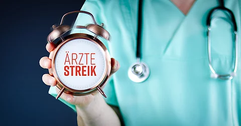 Ärztestreik. Arzt zeigt Wecker/Uhr mit Text. Hintergrund blau.
