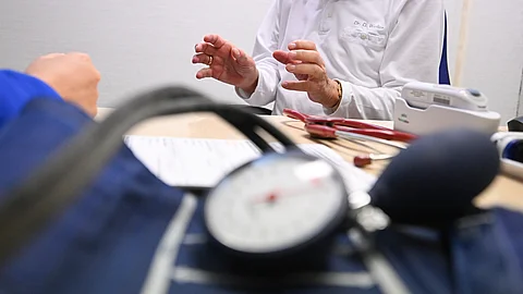 Ein Arzt spricht in einer Bereitschaftspraxis in einem Krankenhaus in einem Untersuchungsraum mit einer Patientin (gestellte Szene). Im Vordergrund liegt Blutdruckmessgerät.