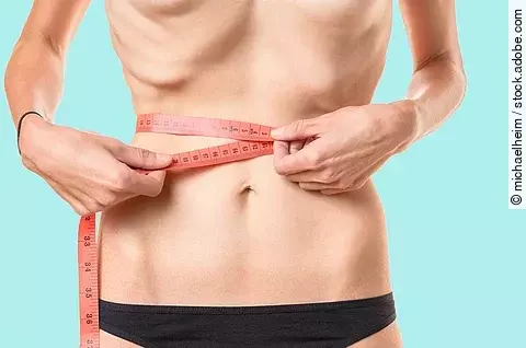 Untergewichtige junge Frau, die ihre Taille mit einem Maßband misst, mit hervorstehenden Rippen und Hüftknochen