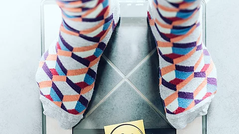 close-up of person in socks on bathroom scale with unhappy smiley face, overweight concept Sockige Füße auf Waage