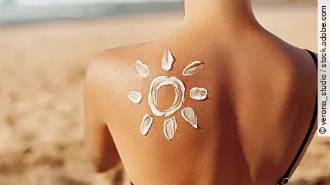 Oberer Rücken einer Person am Strand, auf dem mit Sonnencreme ein Sonnensymbol aufgetragen wurde.