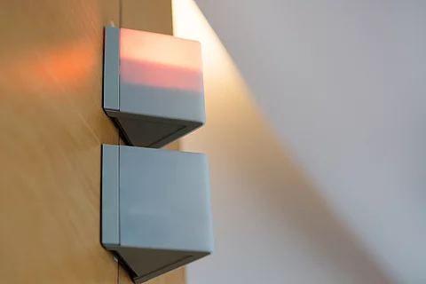 Zwei kantige Signalleuchten an einer Holzvertäfelung, die obere leuchtet rot – Symbol für Alarm oder Besetztanzeige in einem Krankenhaus.