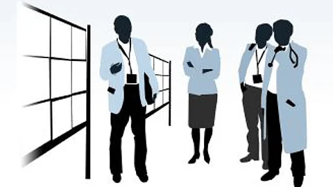 Stilisierte Illustration von vier medizinischen Fachkräften im weißen Kittel mit Stethoskopen und Akten, die in einem Krankenhausgang stehen; im Hintergrund ist links ein großes Fenster mit schwarzem Rahmen sichtbar, die Figuren sind in gedeckten Blau- und Grautönen dargestellt.