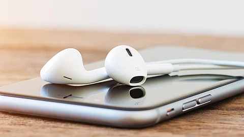 Ein Smartphone liegt auf einem Holztisch, darauf ein Paar kabelgebundene Kopfhörer. 