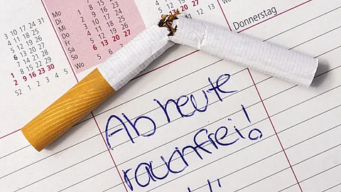 Auf einem Kalender liegt eine zerbrochene Zigarette. Darunter steht handschriftlich „Ab heute rauchfrei“ mit einem Smiley