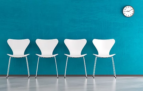 Wartebereich, Stuhlreihe aus weißen Stühlen vor blauer Wand