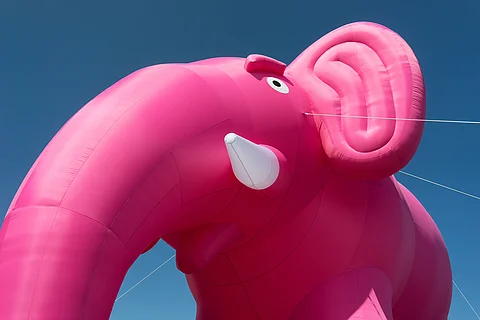 Ein großer rosafarbener aufblasbarer Elefant vor blauem Himmel, detailreich mit Auge und Rüssel sichtbar.