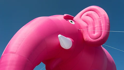 Ein großer rosafarbener aufblasbarer Elefant vor blauem Himmel, detailreich mit Auge und Rüssel sichtbar. Ein großer rosafarbener aufblasbarer Elefant vor blauem Himmel, detailreich mit Auge und Rüssel sichtbar.