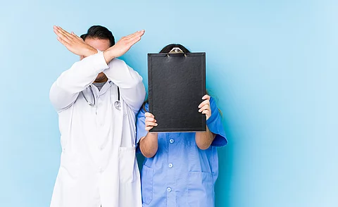 Young doctor couple posing in a blue background isolated keeping two arms crossed, denial concept.