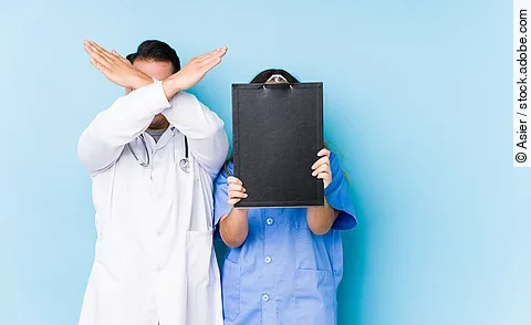 Young doctor couple posing in a blue background isolated keeping two arms crossed, denial concept.