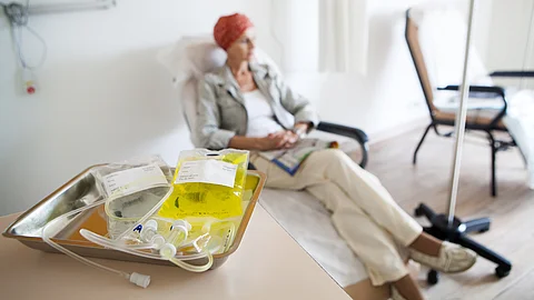 Ambulante Chemotherapie: Im Vordergrund liegen Chemotherapie-Infusionsmaterialien auf einem Tablett, im Hintergrund sitzt eine Patientin mit Kopftuch entspannt in einem Behandlungsstuhl während der Therapie. Ambulante Chemotherapie: Im Vordergrund liegen Chemotherapie-Infusionsmaterialien auf einem Tablett, im Hintergrund sitzt eine Patientin mit Kopftuch entspannt in einem Behandlungsstuhl während der Therapie.