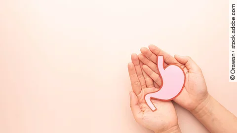 Human hands holding stomach organ made from paper on beige background. Concept of gastric cancer screening, stomach transplant, digestive tract problem and stomach disease treatment. Flat layout.