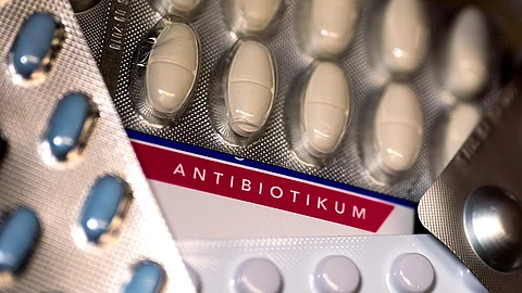 Nahaufnahme mehrerer Blisterpackungen mit Antibiotika-Tabletten in unterschiedlichen Farben. Im Hintergrund ist das Wort „Antibiotikum“ auf einer Verpackung deutlich sichtbar. Blister mit Medikamenten, unter anderem Antibiotik