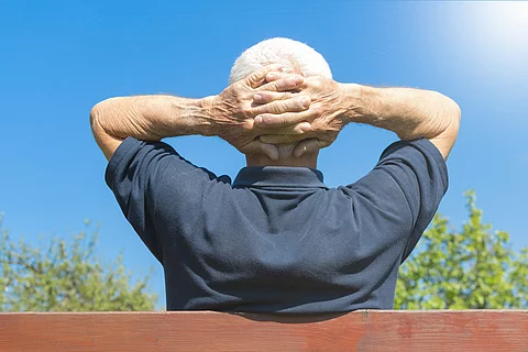Grauhaariger Mann mit verschränkten Armen auf einer Parkbank