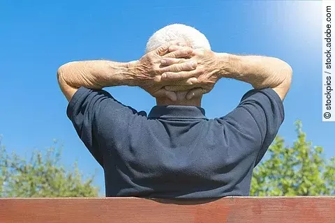 Grauhaariger Mann mit verschränkten Armen auf einer Parkbank