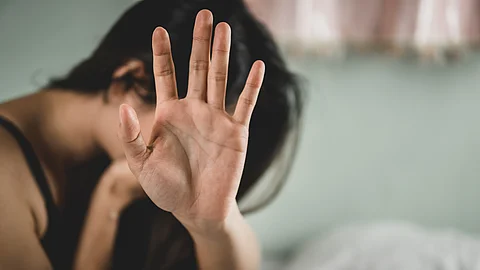 Eine Person sitzt vornübergebeugt auf einem Sofa, hält den Kopf und macht eine abwehrende Geste mit der Hand
