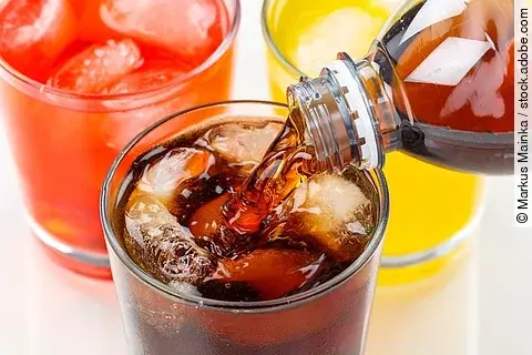 Cola wird in ein Glas eingegossen, das neben zwei anderen Limonadegläsern steht