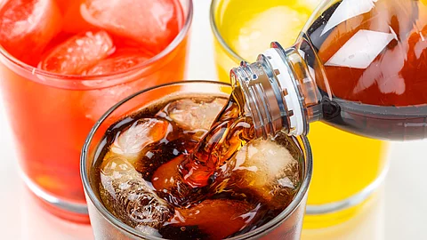 Cola wird in ein Glas eingegossen, das neben zwei anderen Limonadegläsern steht