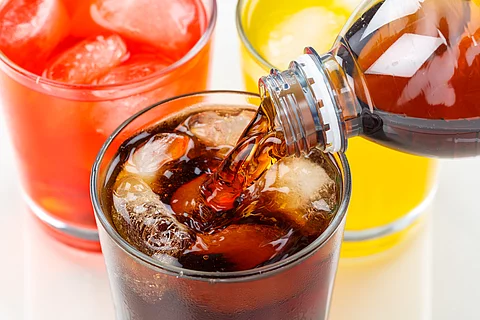 Cola wird in ein Glas eingegossen, das neben zwei anderen Limonadegläsern steht