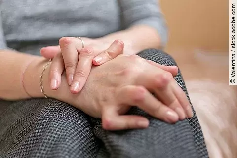 Young woman having rheumatoid arthritis takes a rest sittinng on the couch. Hands and legs are deformed. She feels pain. Selected focus.