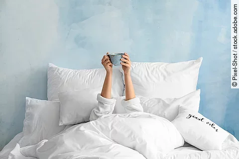 Young woman with cup of hot beverage lying in bed