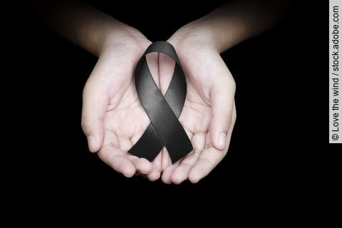 Hand holding black ribbon on black background mourning awareness