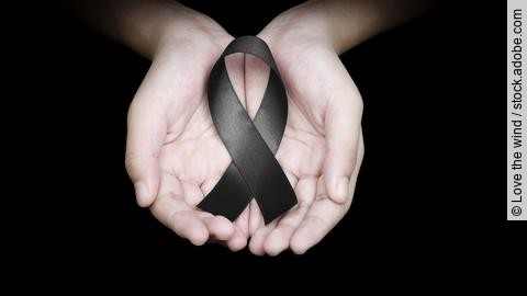 Hand holding black ribbon on black background mourning awareness